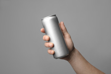 Man holding aluminum can with beverage on grey background, closeup. Space for design