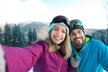 Happy couple taking selfie during winter vacation in mountains