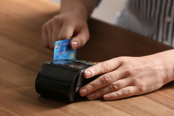 Woman using modern payment terminal at table indoors, closeup