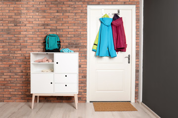 Stylish hallway interior with chest of drawers and clothes hanging on white door