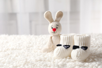 Fototapeta premium Handmade baby booties and stuffed rabbit on plaid against blurred background. Space for text