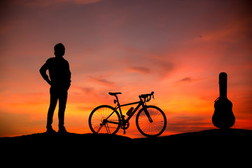 Silhouette young men with guitar and bicycles at sunset
