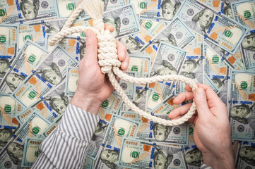 Men's hands with loop of rope on background of dollars. top view