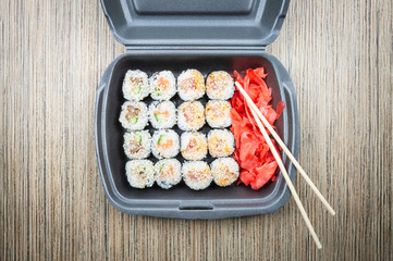 Sushi rolls in a container on a wooden table. top view,
