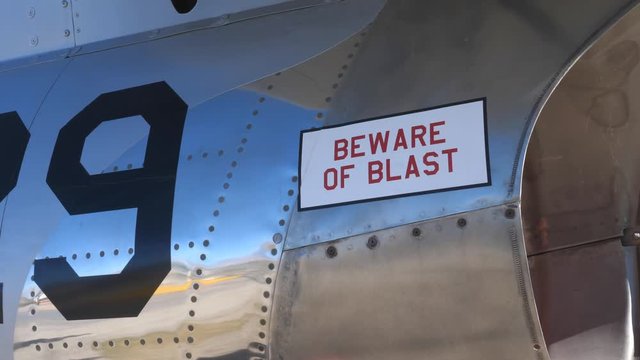 Tilt up to BEWARE of BLAST near engine of 1950s fighter jet. F-86 Sabre. Handheld shot with stabilized camera.
