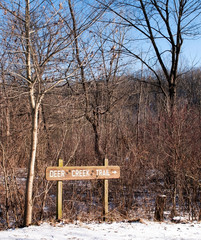 January, 31, 2019 Pittsburgh, Pennsylvania, USA The Deer Creek Trail sign in lower Frick Park on a bright winter day with blue skies and bare trees in the background