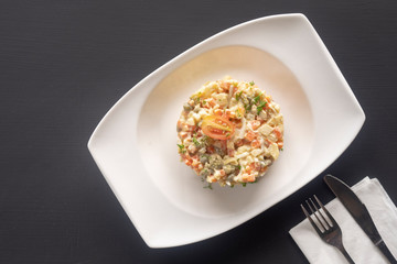 olivier salad on a white plate on a dark background