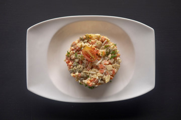 olivier salad on a white plate on a dark background
