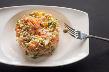 olivier salad on a white plate on a dark background