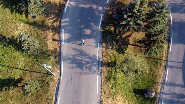 drone footage from above of a man skateboarding down a hill on a very bendy road with lots of turns, filmed in the evening with a golden glow to the picture
