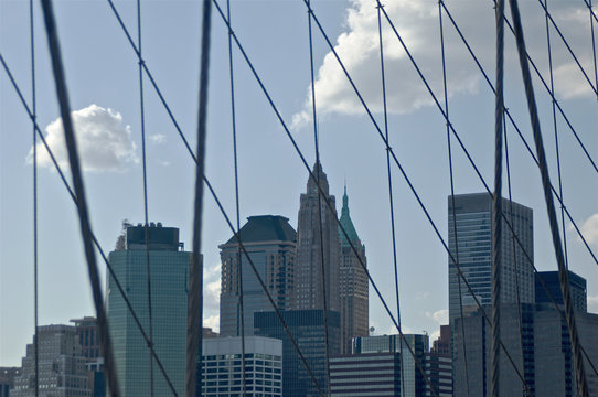 Fototapeta A cluster of buildings situated in New York City's lower Manhattan as seen through the high-tension wires of the iconic Brooklyn Bridge.