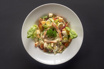 Caesar salad on a white plate on a dark background.