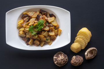 fried potatoes with mushrooms on a white plate on a dark background