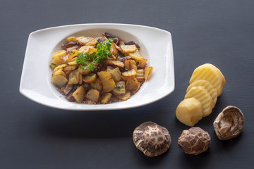 fried potatoes with mushrooms on a white plate on a dark background