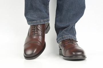 Male legs in jeans and brown classic shoes on white background