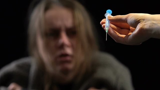 Dealer hand offering syringe with dose to woman with withdrawal, addiction