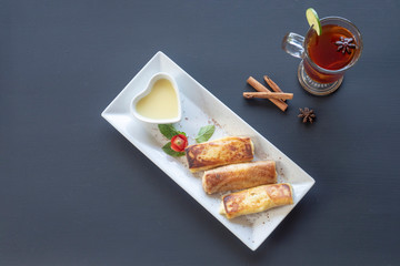 Pancakes on a white plate with tea, spices, lemon and cinnamon on a dark background