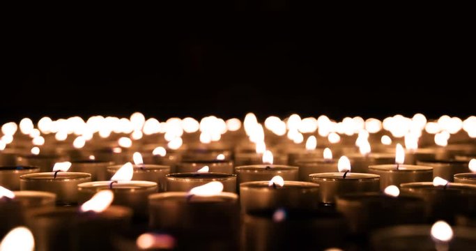 Field of Burning Candles to Horizon. Many small burning candles create a fiery carpet to the horizon in absolute darkness. Wind blows out the candles