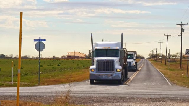 3 Bottom belly dump trucks in convoy  turning at a junction in remote rural area of Texas