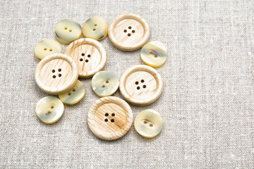 Large wooden and a small mother of pearl sewing buttons on light natural linen fabric 