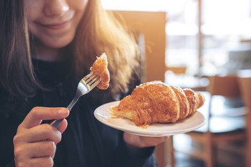 Closeup image of hands cutting a piece of croissant by fork to eat on wooden table