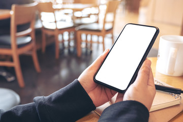 Mockup image of hands holding black mobile phone with blank white screen in cafe