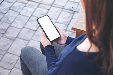 Mockup image of a woman holding black mobile phone with blank white screen while sitting in the outdoors