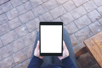 Top view mockup image of a woman holding black tablet pc with blank white screen while sitting in the outdoors