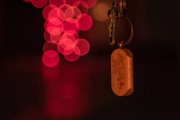 An underexposed wooden crafted keyring quoting CITY OF MUSSORIE accompanied with the soft blurry pink bokeh of Christmas lights 