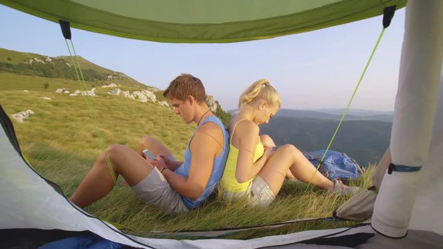 SLOW MOTION, CLOSE UP Young tourist couple addicted to their smartphones texting during a hiking trip. Millennials not enjoying the picturesque sights of the Alps and browsing the internet instead.