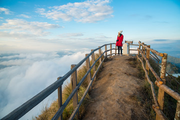 Tourist woman standing and looking view on the highest peak of Phu Chi Dao mountain in Chiang Rai province of Thailand. (The Thai language on the wooden sign post is the name of this place)