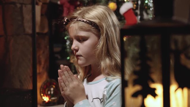 A small young girl kneels by her fire place and says a prayer of peace and goodwill at Christmas time.