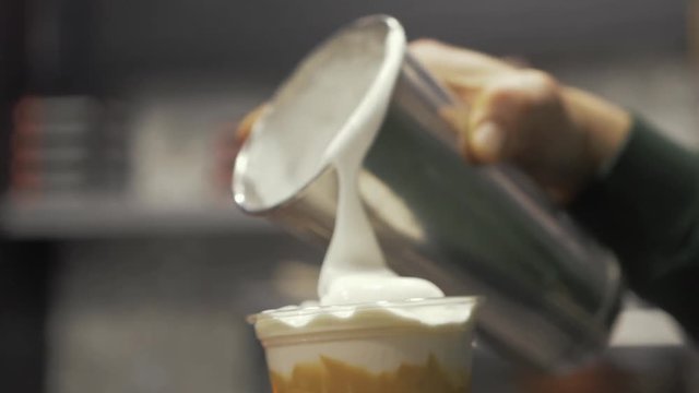 Barista pouring frothy milk over freddo cappuccino in slow motion