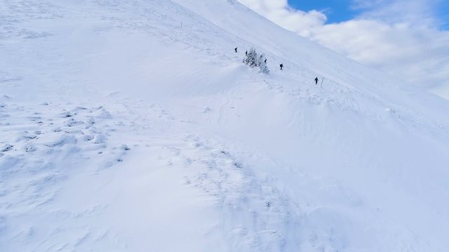Aerial, tracking, drone shot, ofa group of people, hiking down from the snowy, Botev peak, in Balkan mountains, on a winter day, in Central Balkan National Park, Bulgaria