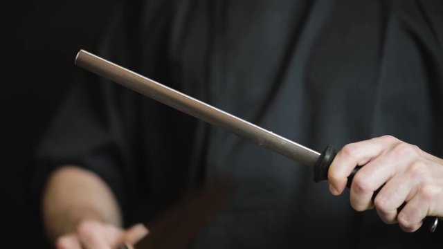 Close-up of male hands sharpening a knife blade on a black background