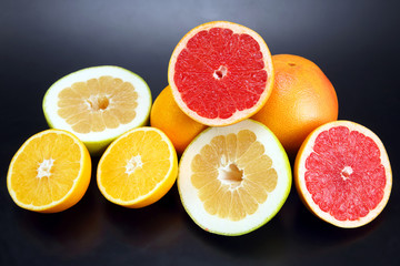 cut pieces of different citrus fruits on dark background