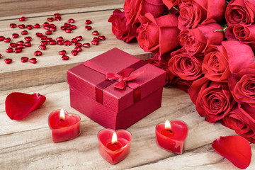 Festive background to the Valentine's day. A bouquet of red roses, a gift box and a heart-shaped candle. On a wooden background.