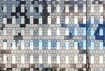 The facade of a modern high-rise building. Front view of many windows. Wall of various shades of gray. Perfect for urban background and design.