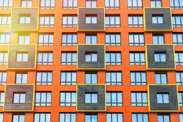 Fototapeta na wymiar The facade of a modern high-rise building. Front view of many windows. Black squares with a yellow border against a bright orange wall. Perfect for urban background and design.