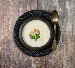 Champignon mushroom cream soup in bowl on wooden background. Rustic style. Top view.