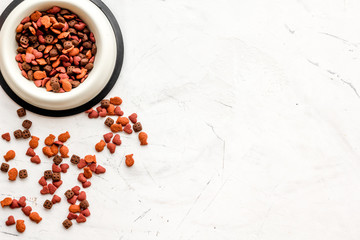 Dry cat food in bowl on white stone backgorund top view copy space