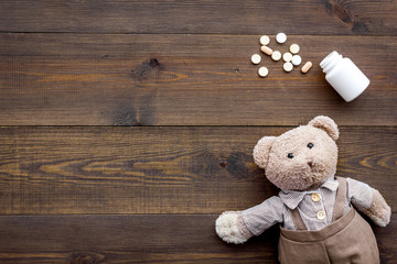 Childhood diseases concept. Treatment of children.Teddy bear toy and pills on dark wooden background top view space for text