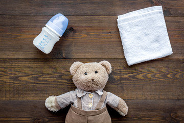 Feed baby concept. Teddy bear toy near small bottle with food on dark wooden background top view
