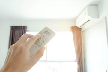 Man's hand using remote control open The air conditioner is cooled to 25 degrees Celsius in his bedroom. Health concepts and energy savings