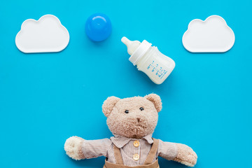 Feed baby concept. Teddy bear toy near small bottle with food on blue background top view copy space