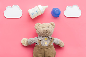Feed baby concept. Teddy bear toy near small bottle with food on pink background top view copy space