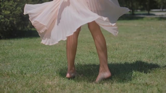 slow motion low angle shot girl barefoot figure dances spinning and pink dress skirt fans on summer park green grass