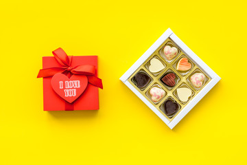 Gift for Valentine's day. Gift box with text I love you and heart-shaped sweets on yellow background top view space for text