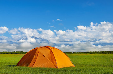 The orange tent on the meadow with foggy mountains on background © Asya