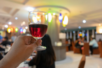 The male hand is holding a glass of wine with a drink in celebration with people in the event that enjoys a holiday lifestyle in a romantic atmosphere.